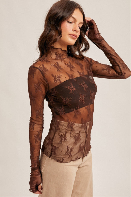 Woman wearing a brown lace top and beige pants against a plain background