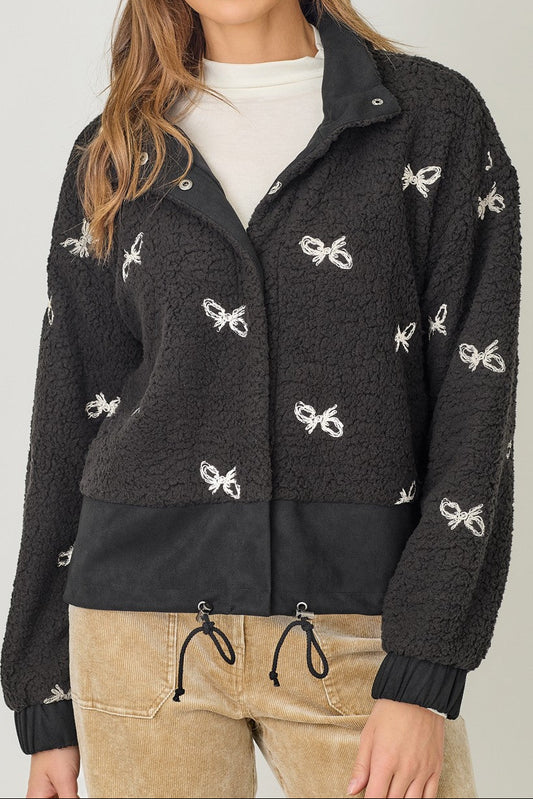 Woman wearing a black jacket with white bow patterns on a plain background