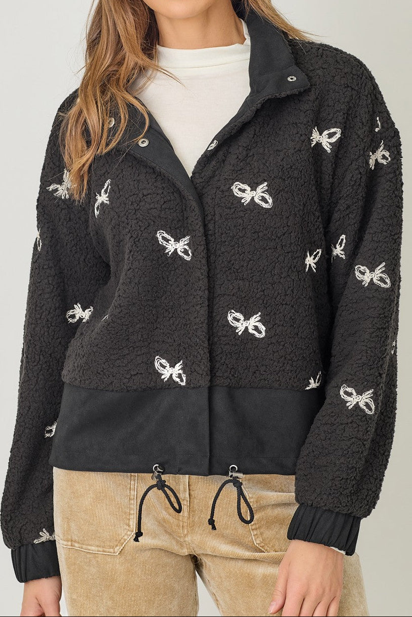 Woman wearing a black jacket with white bow patterns on a plain background