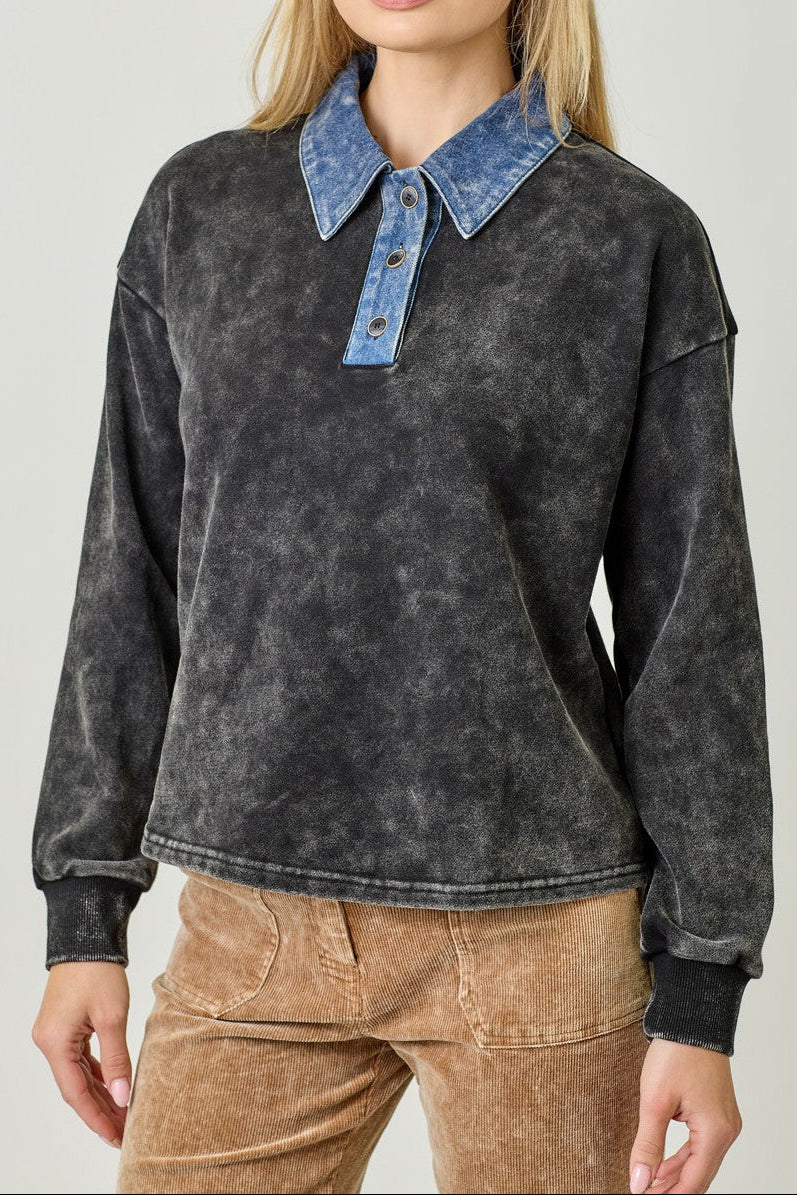 Woman wearing a dark acid-wash pullover with a denim collar against a plain background