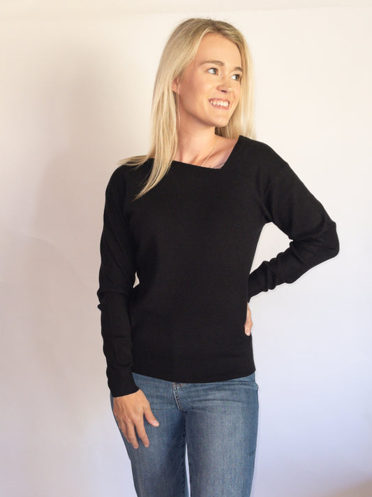 Woman wearing a black Asymmetrical Sweater and blue jeans against a plain background