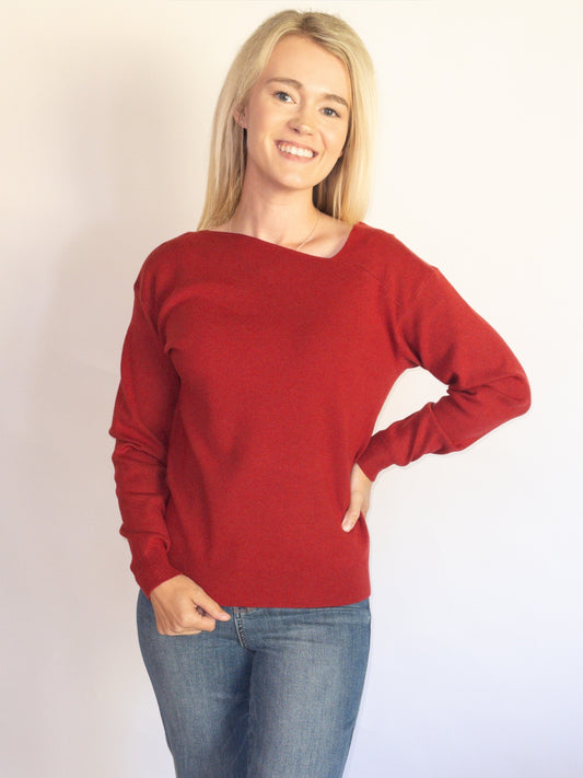 Woman wearing a red Asymmetrical sweater and blue jeans against a plain background