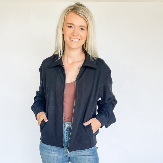 Woman wearing a black suede jacket over a brown top and blue jeans against a white background