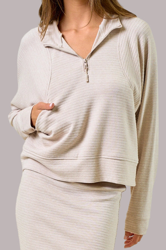 Woman wearing a beige long-sleeve top with a zipper on a light green background