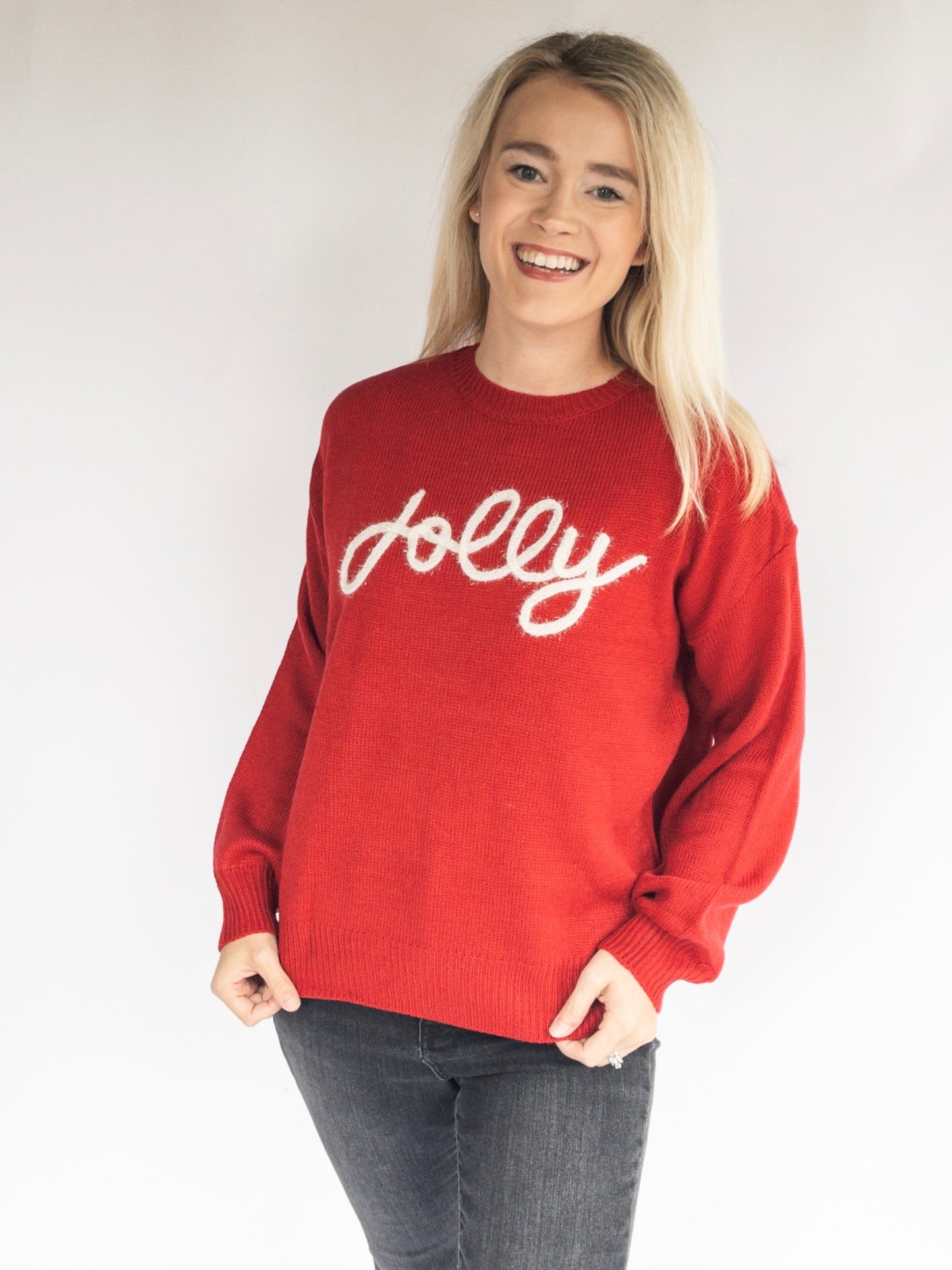 woman wearing a red christmas sweater with 'Jolly' text on a plain background