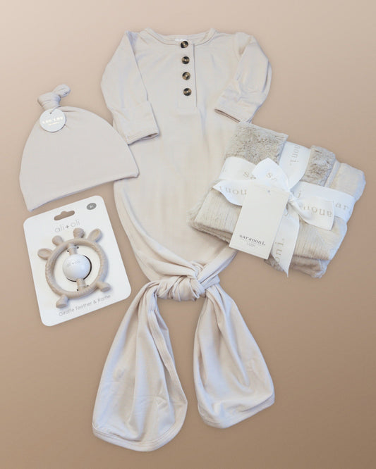 Lou Lou & Company Winnie Gown + Hat clothing and accessories set including a onesie, hat, swaddle, and teether on a beige background.