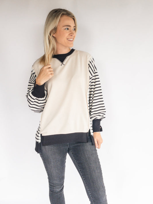 Woman wearing a striped sweatshirt and gray jeans against a white background