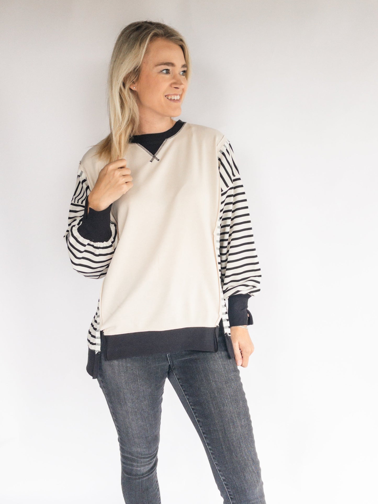 Woman wearing a striped sweatshirt and gray jeans against a white background