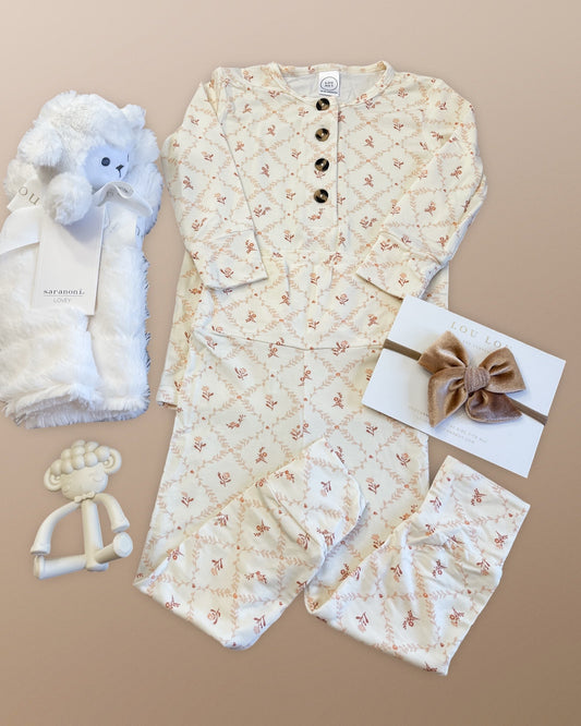 Lou Lou & Company Annie outfit with floral pattern, Saranoni Lamb Lovey blanket, and  sheep teether and bow on a beige background