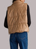 Woman wearing a beige puffer vest and blue jeans on a plain background