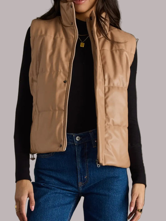 Woman wearing a beige vest over a black shirt and blue jeans on a gray background