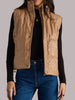 Woman wearing a beige vest over a black shirt and blue jeans on a gray background